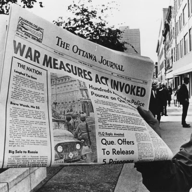 A black-and-white photograph showing a young man holding up a newspaper titled "The Ottawa Journal" with the headline "WAR MEASURES ACT INVOKED" and subheadlines about hundreds of police on Quebec streets and the nation being laughed at. The background features a city street with buildings, trees, and several people walking or standing.