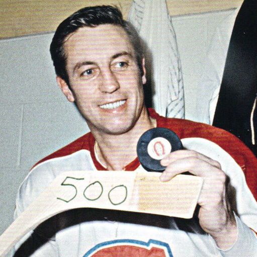 The photo shows Jean Béliveau in a Montreal Canadiens hockey jersey, smiling and holding a hockey stick with the number 