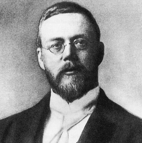 A black-and-white photograph of a man with a full beard and mustache, wearing glasses, a high-collared white shirt, and a dark suit jacket with a vest. He has a serious expression and is photographed against a plain background. The signature "Reginald A. Fessenden" is written in the bottom right corner.