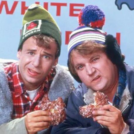 Two men, Bob and Doug McKenzie, wearing winter hats and coats, holding donuts and sitting in front of a "White" sign with a map outline.