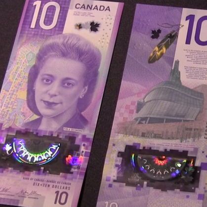 The photo shows two Canadian $10 bills side by side. The bill on the left features a portrait of a woman with styled hair, alongside a map-like design. The bill on the right displays an image of a modern building, possibly a cultural or governmental structure, with a feather element. Both bills have holographic security strips with colorful, shifting patterns, and include the denomination "10" prominently. The background is dark, highlighting the bills' vibrant colors and details.