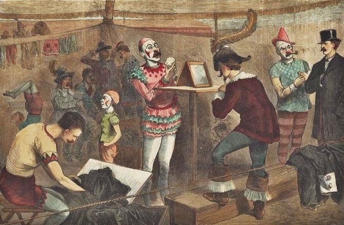 The image depicts a vintage scene inside a circus tent, featuring several individuals dressed in colorful, theatrical costumes. A central figure, a clown with a white face, red nose, and green-and-pink ruffled outfit, stands holding a small mirror. Surrounding the clown are other performers, including a man in a maroon outfit adjusting his appearance, another clown in a blue-and-red costume, and a person in a top hat and formal attire. In the foreground, a performer in a yellow-and-red outfit is working with a large black cloth or costume piece. The background shows additional circus performers and props, including hanging costumes and a lively, crowded atmosphere. The overall style suggests an old illustration, possibly from a 19th-century circus or theatrical setting.