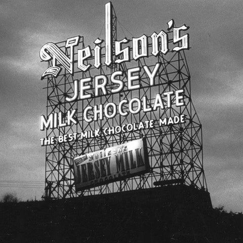 A black-and-white photograph of a large vintage billboard advertising Neilson's Jersey Milk Chocolate. The billboard features bold, stylized text with 