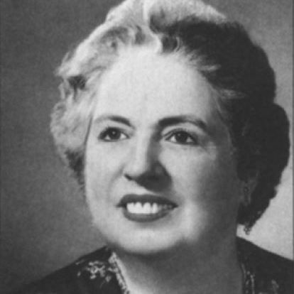 Black-and-white portrait of Dorothea Palmer, an older woman with light, wavy hair in an updo. She smiles gently at the camera, wearing a dark floral-embroidered blouse and beaded necklace. Head-and-shoulders shot on plain background.