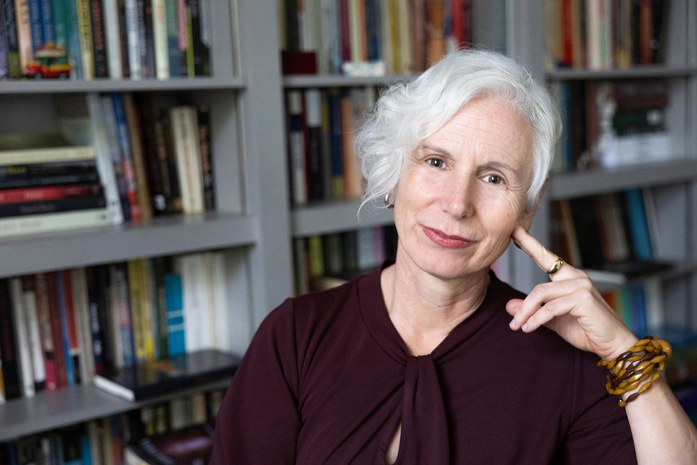 Yanna Yannakakis, professor and chair of Emory College Department of History, smiles and touches her cheek with one hand while seated in front of a full bookshelf.