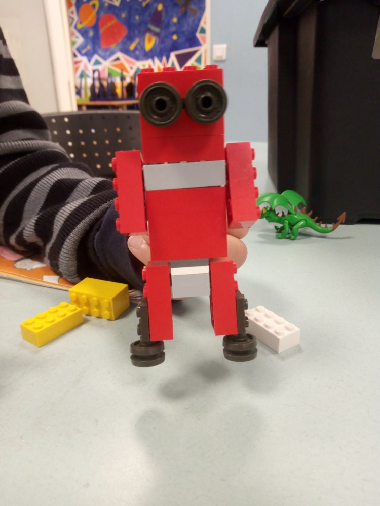 robot lego, rouge, ses yeux c'est des pneus, tenu par une main d'enfant