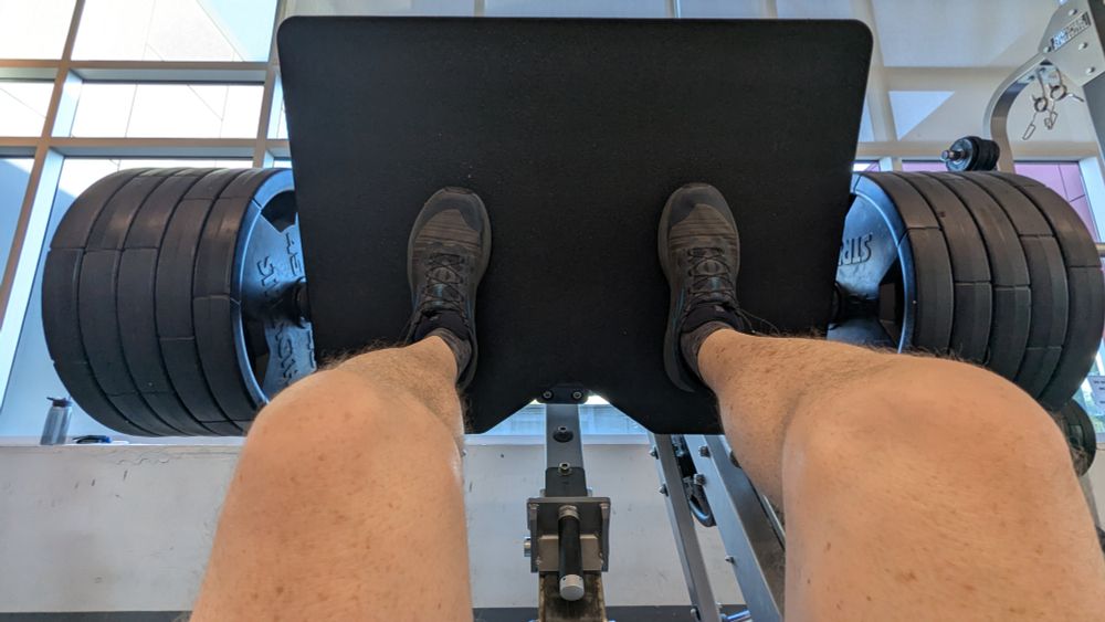 An image of a leg press machine at a gym with 10 45 lbs plates and a pair of legs pushing against the machine.  