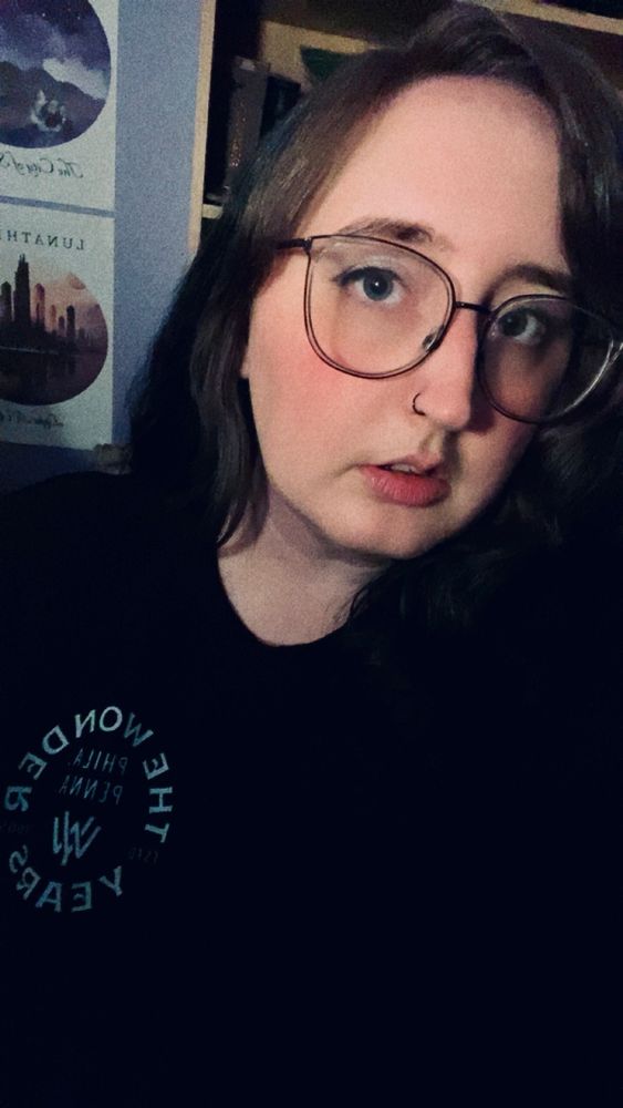 selfie of me wearing a black the wonder years sweater, large glasses, with dark hair and silvery eye makeup and black eyeliner