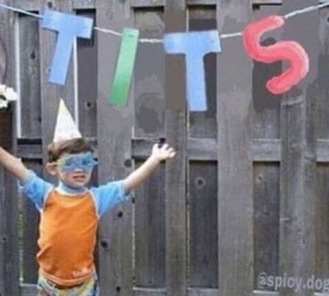 a child standing in front of a fence and there's party decorations behind him but it looks like it just says TITS and he's holding his arms up