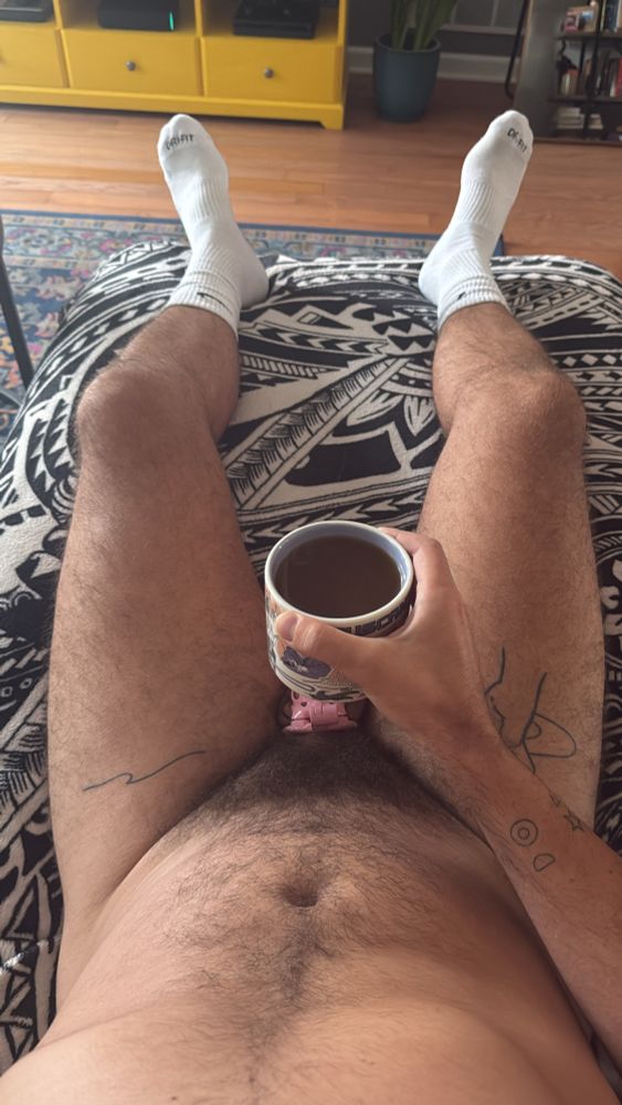 POV down at nude body on couch wearing socks and cage holding coffee mug slightly over caged cock for censorship 