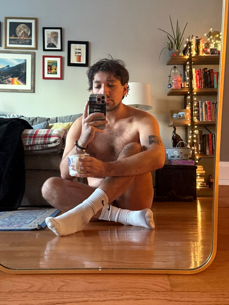 Naked in white Nike socks on the floor crossing legs holding coffee cum 