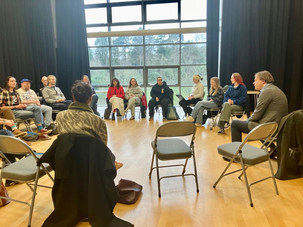 A group of people seated in a circle in a studio space.