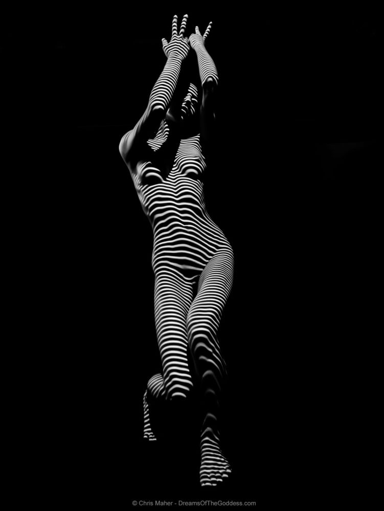 a photograph of a woman in a yoga pose wearing only stripes of light and shadow.