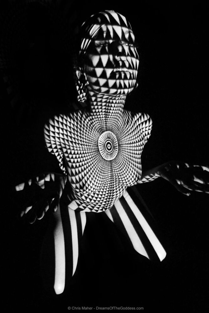 A black and white pattern is projected upon her as she kneels on the floor..