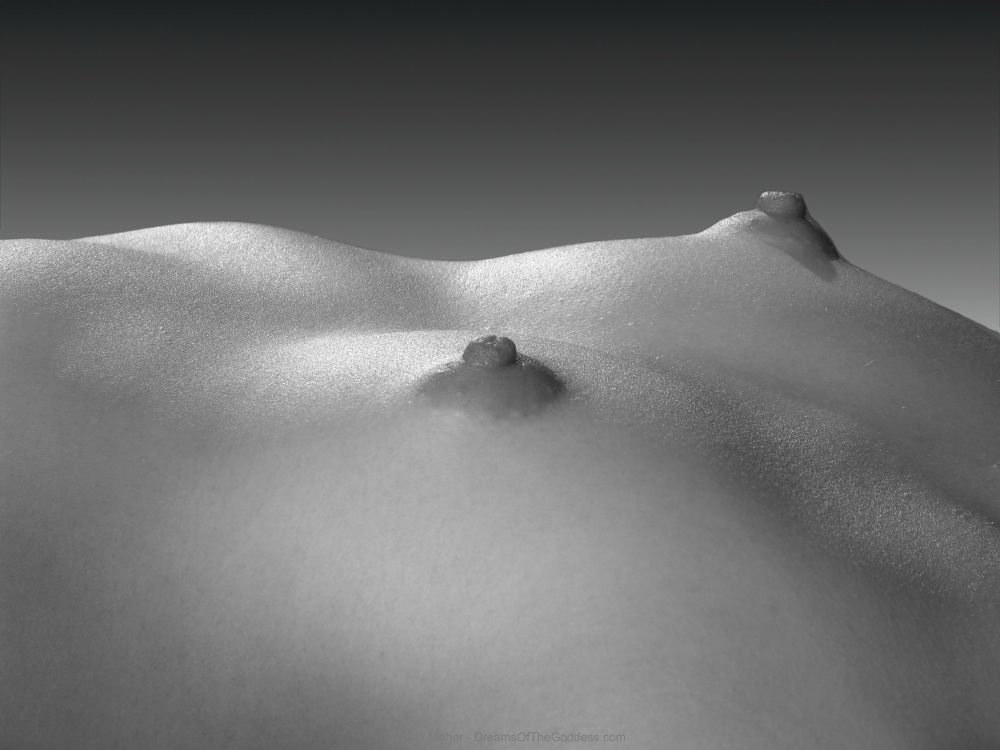 This is a close-up photograph of a young woman’s nude breasts as she is lying down. She is flat chested with large nipples.