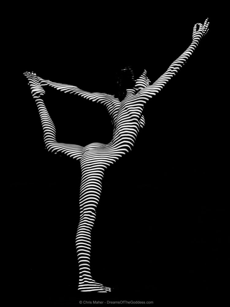 a photograph of a woman in a yoga pose wearing only stripes of light and shadow.
