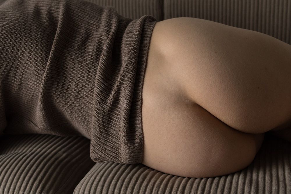 A is woman lying on a sofa with her back to us, nude from the waist down. The crop reveals her only from mid-back to the start of her thigh. The texture and colour of her top matches the sofa, curiously enough.