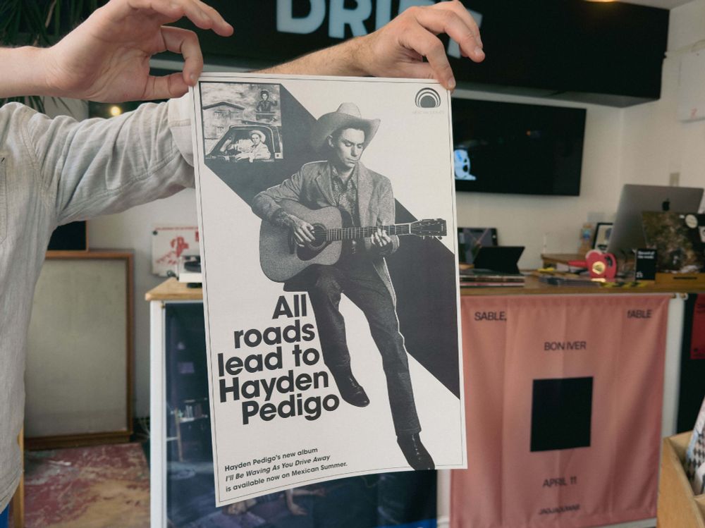 A photo of hands holding a Hayden Pedigo poster in the shop at Drift Records.