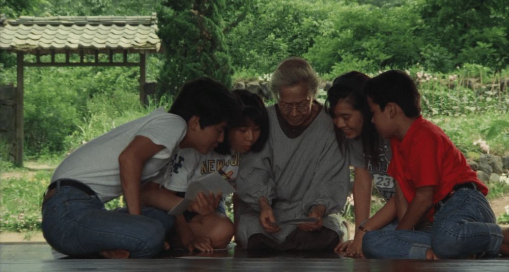 Four Japanese youth sit on veranda, reading a letter with their grandmother in traditional dress. Scene from Kurosawa's Rhapsody in August.