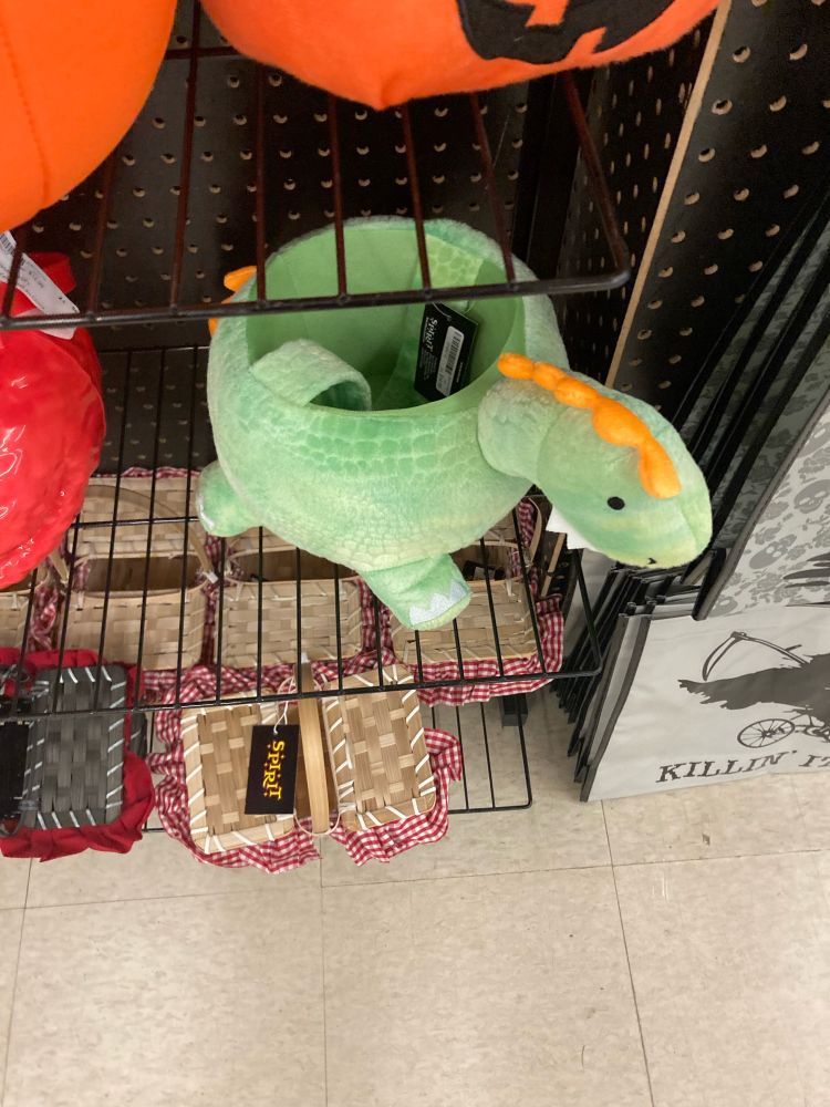 A Halloween trick or treat basket shaped like a green dinosaur with orange back plates