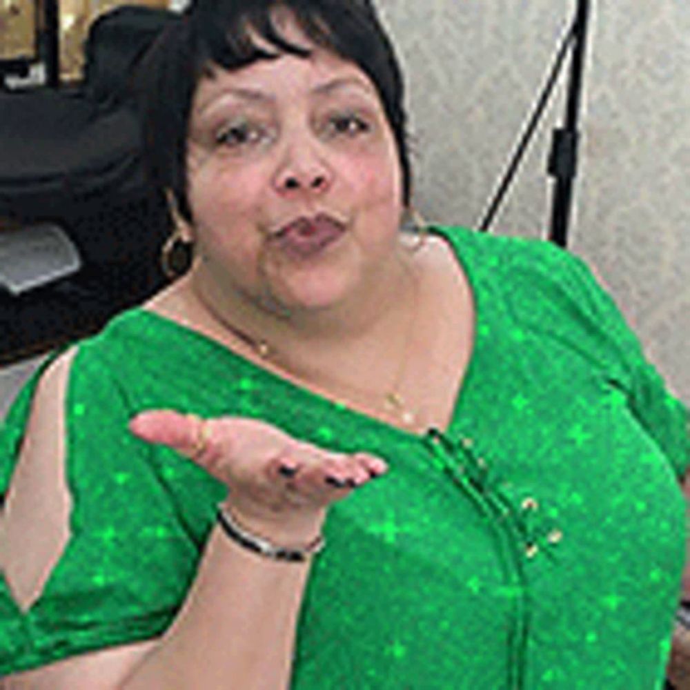 a woman in a green shirt is blowing a kiss while standing in front of a printer .