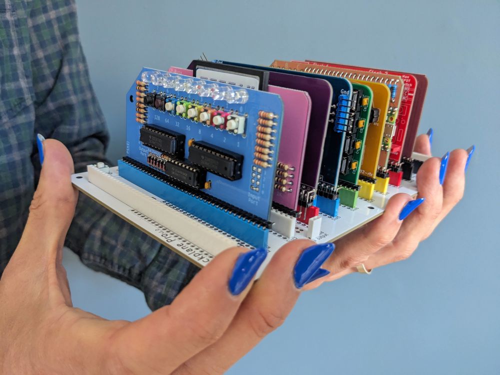 An assembled RC2014 Zed Pro modular Z80 hobby computer, which comprises a backplane about the size of a paperback book with playing-card sized component circuit boards plugged into it vertically. This particular Zed Pro is the limited-edition Pride kit, where the component boards are coloured so that they form a rainbow when arranged in the backplane.

The computer rests in the hands that assembled it, which here are sporting some fairly long, blue-varnished fingernails. All of the electronic components, including dozens of resistors, headers, and IC sockets, were placed and soldered with the fingers and fingernails shown.