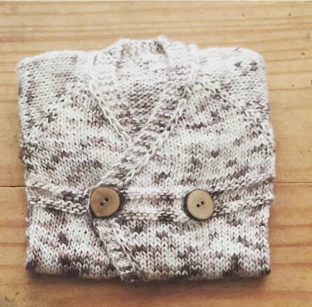 Carina Spencer’s Small Things Romper, folded up for wrapping. This version is knit in brown and white wool. It has brown wooden buttons.