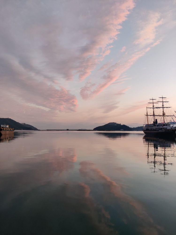 南あわじ市。海に面して夕日が写ってる。奥に島々（四国）、右側にうずしおクルーズの人船が見えてる。紫やピンク色がかった雲が空にも海にも見えます。