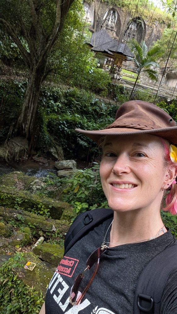 A woman in a cowboy hat taking a selfie in front of an old temple 