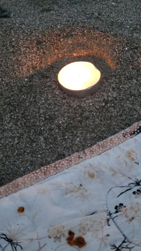 A lit tealight in the sand on a beach