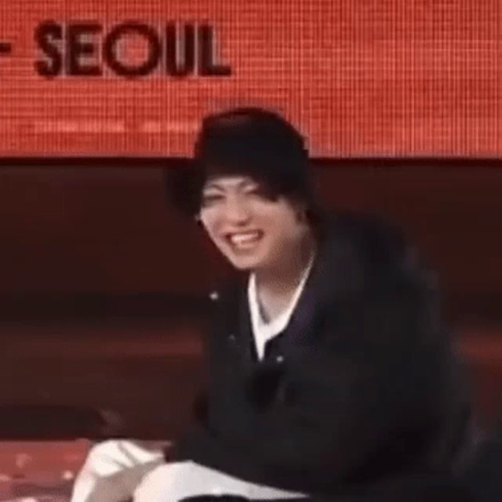 a man wearing a hat and a jacket is sitting on a stage and smiling .