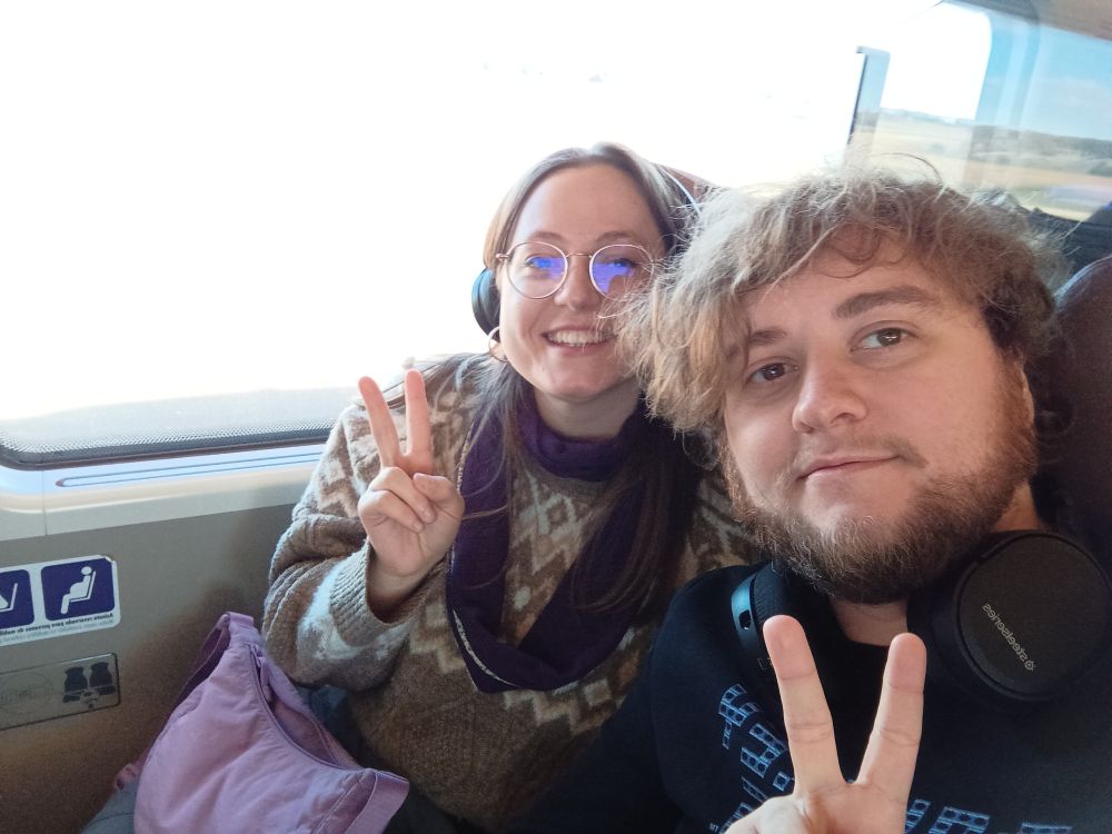 Una dona i un home joves asseguts en un tren fent el signe de la v amb els dits