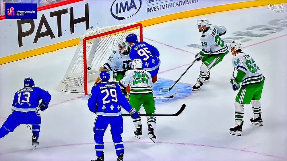 Phot of a TV broadcast of a hockey game between the Colorado Avalanche, dressed in Quebec Nordiques uniforms, and the Carolina Hurricanes, dressed in Hartford Whalers uniforms. 