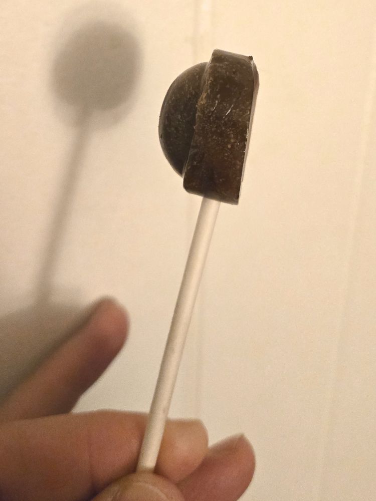A lollipop that was, formerly, spherical with a "band" around the center from "north pole" to "south pole" (where the stick is), now missing an entire hemisphere, and almost perfectly flat on that side.
