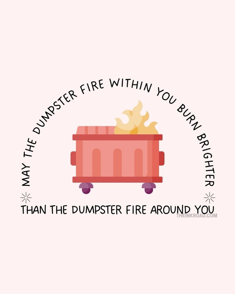 On a pale pink background, a lighter red dumpster with purple wheels is on fire. The words surrounding it read “MAY THE DUMPSTER FIRE WITHIN YOU BURN BRIGHTER THAN THE DUMPSTER FIRE AROUND YOU.” meme by theinkroad.com