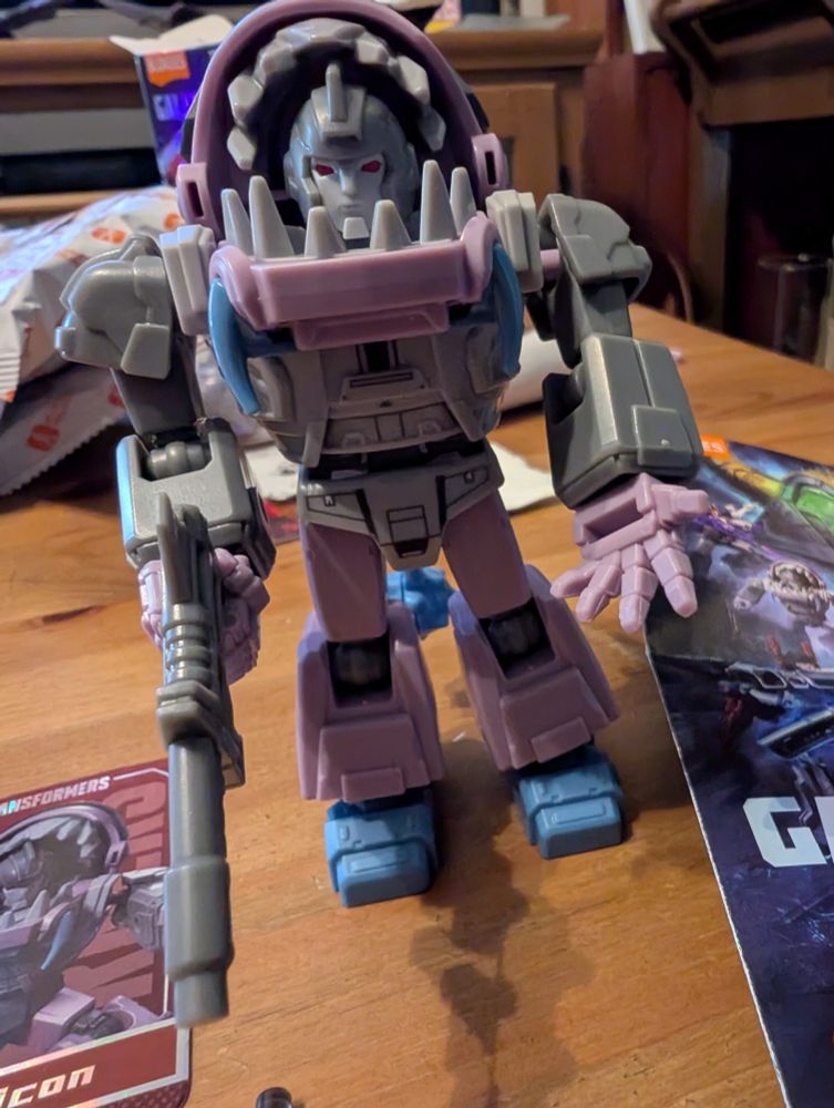 Transformers Gnaw in robot mode from Blokees blind box model kit, constructed. He is a robot form of a little shark guy. He has a gun and has his hand out asking for an energon stick.