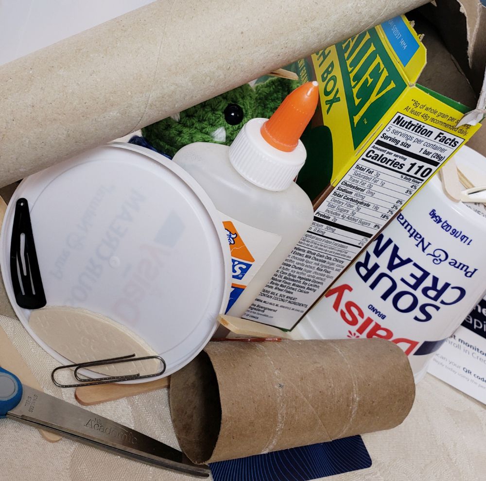 A pile of random items that we will use during my Twitch stream today to make tatting shuttles out of household objects. Some items: cardboard boxes, a sour cream container, toilet paper and paper towel rolls, clothespins, hair clips, and scissors and glue. 