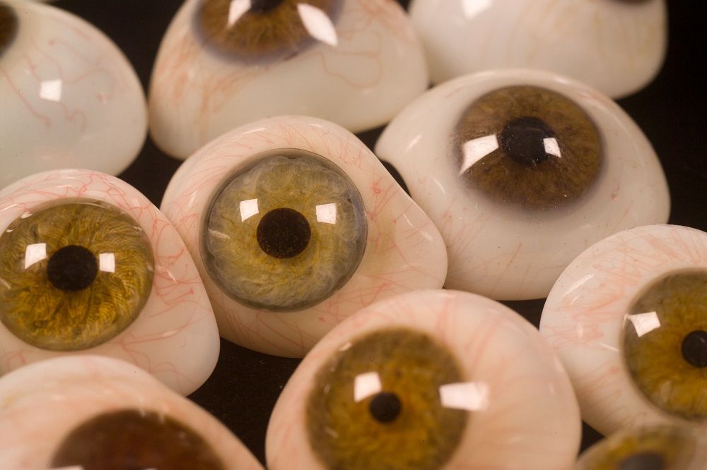 Glass eyes lying on a black background. The eyes are half globes that closely resemble a human eye, including the black pupil, coloured iris (in shades of blue, green and brown) and the white sclera with the details of red blood vessels. 