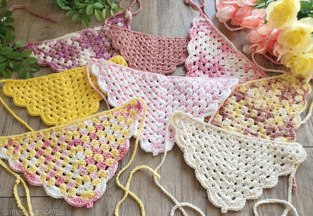 A photo of several handmade crochet bandanas, mostly pink and yellow colored with some solid and some variegated.