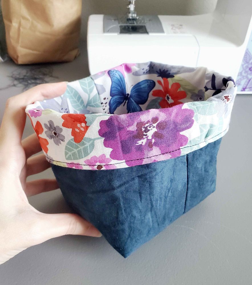 Photo of the basket reversed, with the flowers and butterflies on the inside, with the rim folded out and covering some of the blue fabric. The blue fabric looks like velvet, not sure why, but it's just regular cotton-feeling fabric irl.