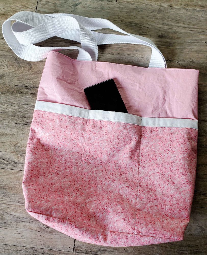 Photo of the opposite side of the bag. The top third is the solid light pink, with the bottom third being the floral pink. However here, there is a white stripe going across the top of the floral pink fabric, and the floral fabric is split into three separate pockets. Again, phone is peeking out of the middle pocket as prop.