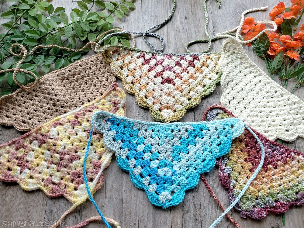A photo of several handmade crochet bandanas, primarily muted colors for fall, like brown, creme, desaturated rainbow, and one blue colored with some solid and some variegated.