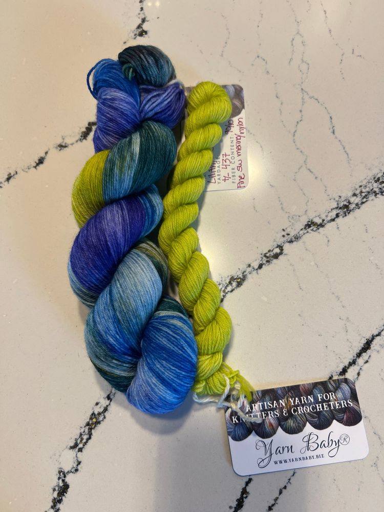 A skein of purple, blue, green with splashes of chartreuse, paired with a mini skein of chartreuse yarn. 