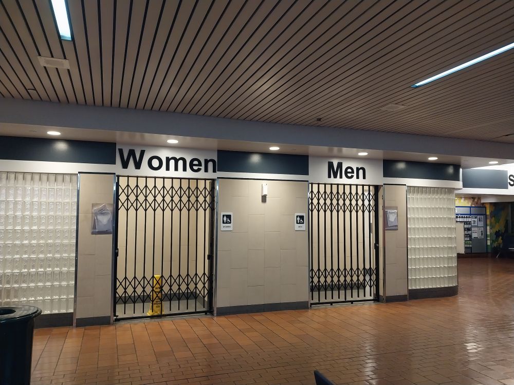 a photo of men's and women's bathrooms with gates drawn across the entrances. the scene is completely devoid of life.