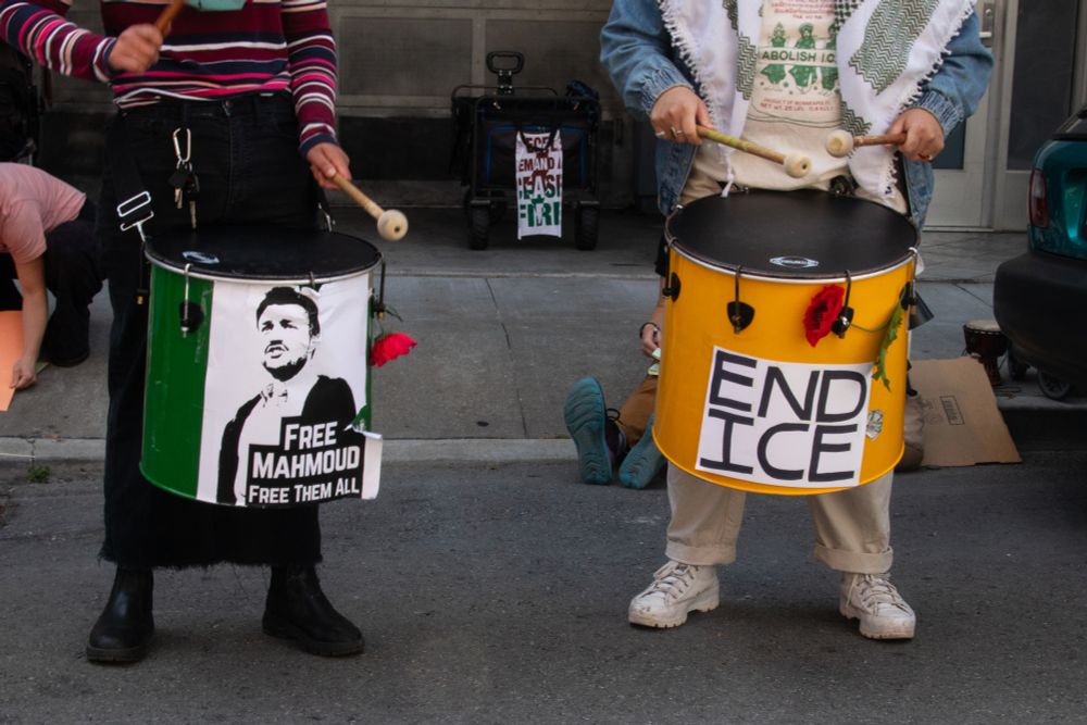 Two tom drums, with signs on them saying "Free Mahmoud, free them all" and "End ICE"