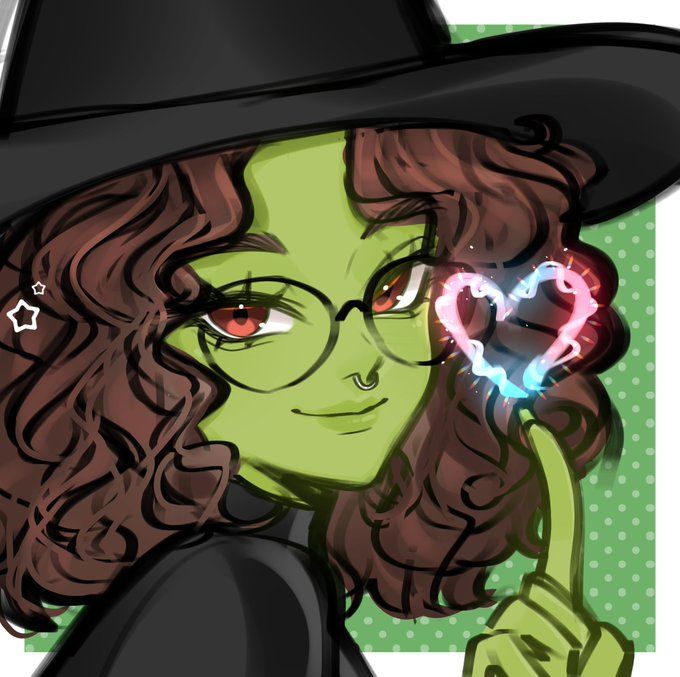 Desenho de uma garota com pele verde, cabelos cacheados castanhos na altura dos ombros, olhos avermelhados, óculos redondos e piercing no septo, olhando em direção à câmera. Ela está vestindo um chapéu preto de bruxa e um vestido preto, como a Elphaba de Wicked. Um de seus dedos está levantando, formando um coração nos tons da bandeira trans com magia.