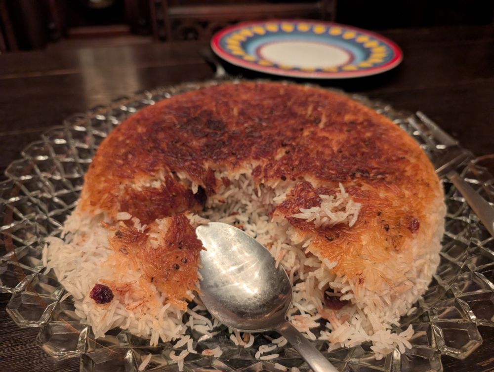 A spoon breaking through a tahdig with perfectly crispy crust on a decorative plate.