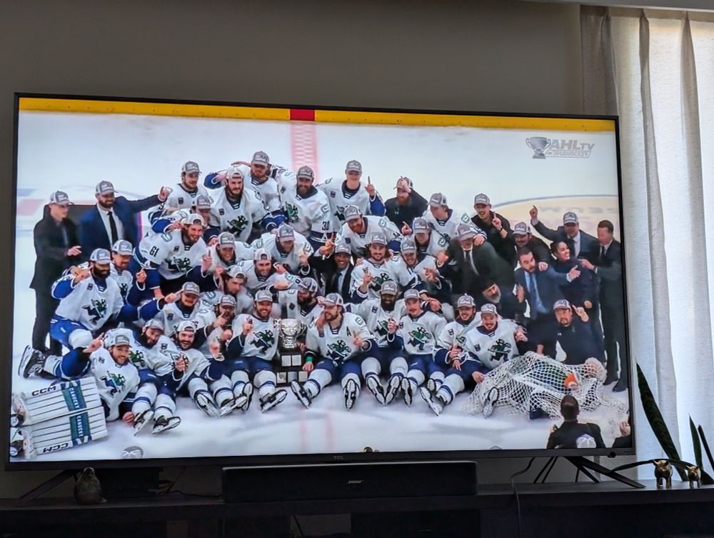 tv screen showing Abbotsford Canucks posing for team photo as 2025 Calder Cup Champions