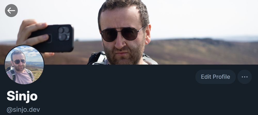 Screenshot of my Bluesky profile, showing the selfie as my profile pic and the wider photo of me taking the selfie as my banner.