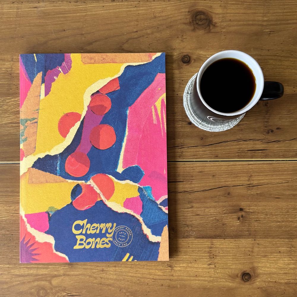 Photo of a magazine called Cherry Bones next to a cup of black coffee on a wooden table